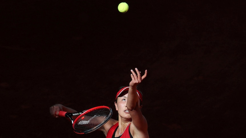 A photo of Peng Shuai serving wearing red with black background.