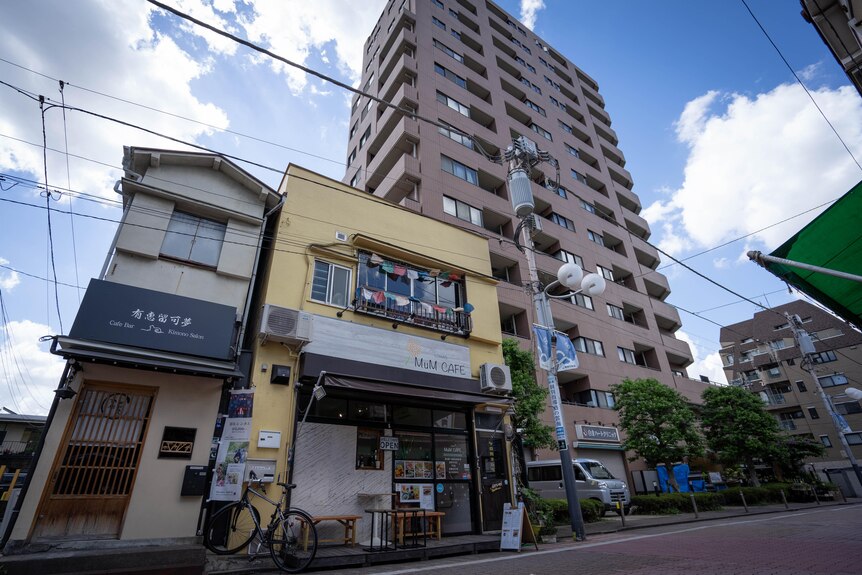 A small cafe front sits next to a tall apartment building on a street.