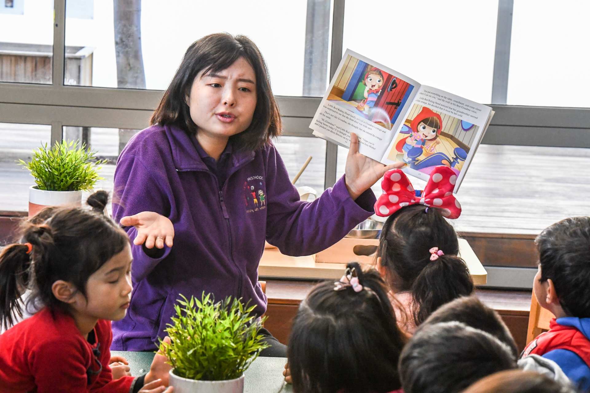 a woman in a purple jumper holds up a picture book with children infront of her