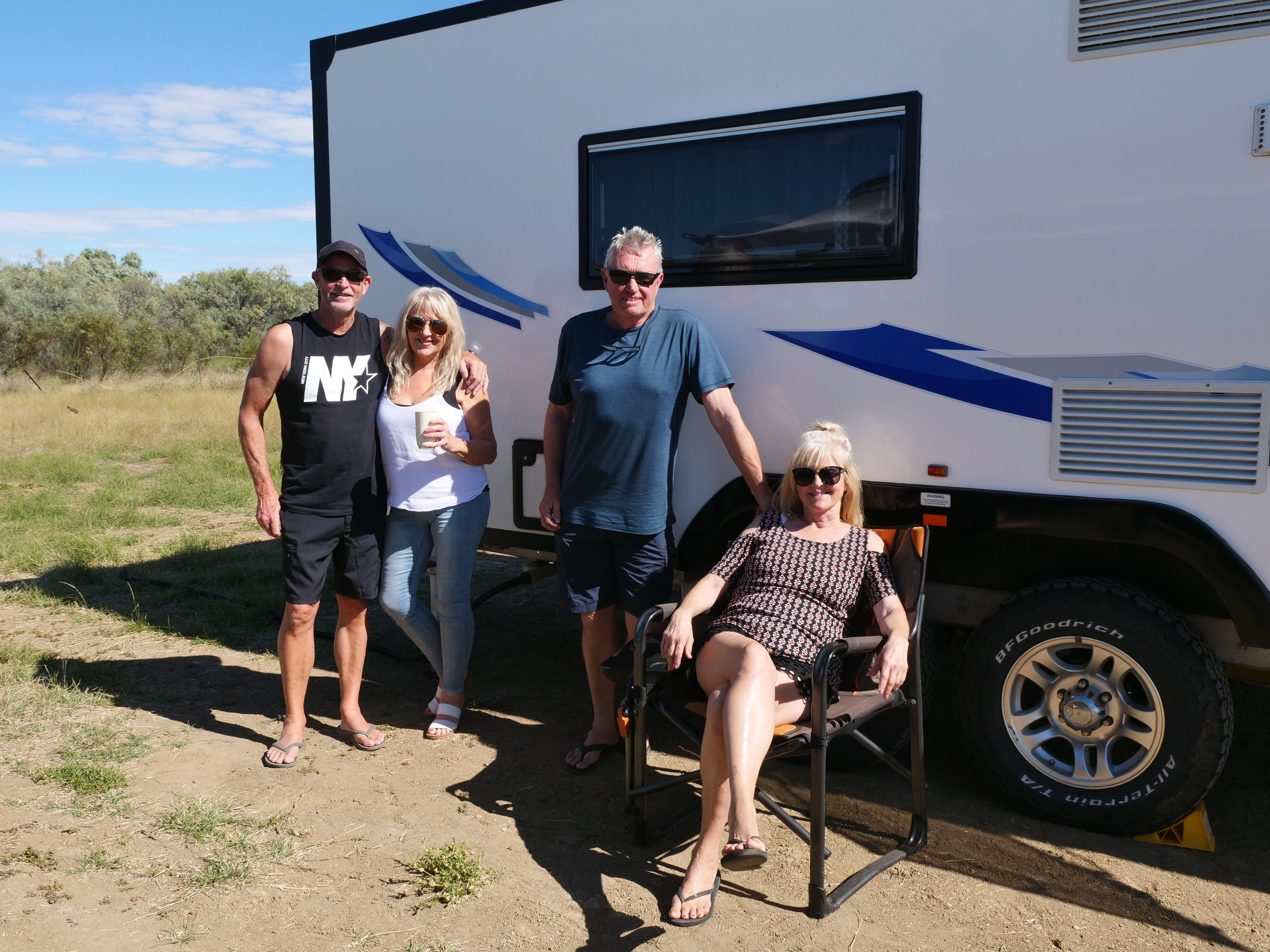 Four travellers smile outside a caravan.