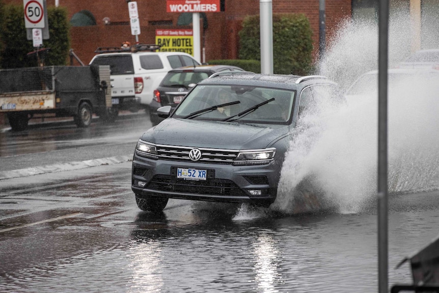 Water sprays up from a road as a car drives through a puddle