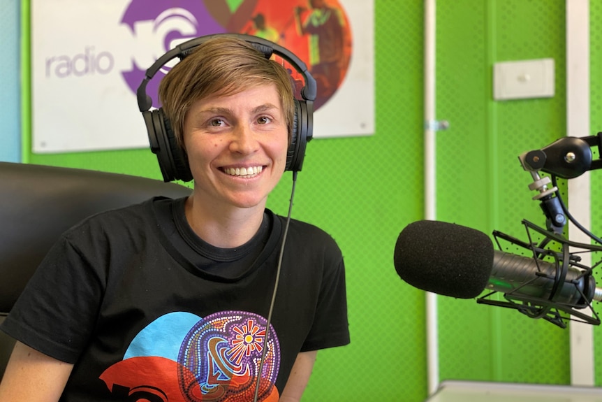 a woman with short hair and a black t shirt in a radio studio 