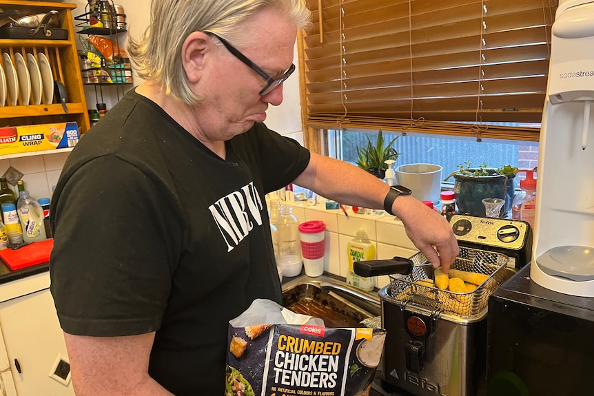 A middle-aged white man frying frozen chicken fingers in a home kitchen