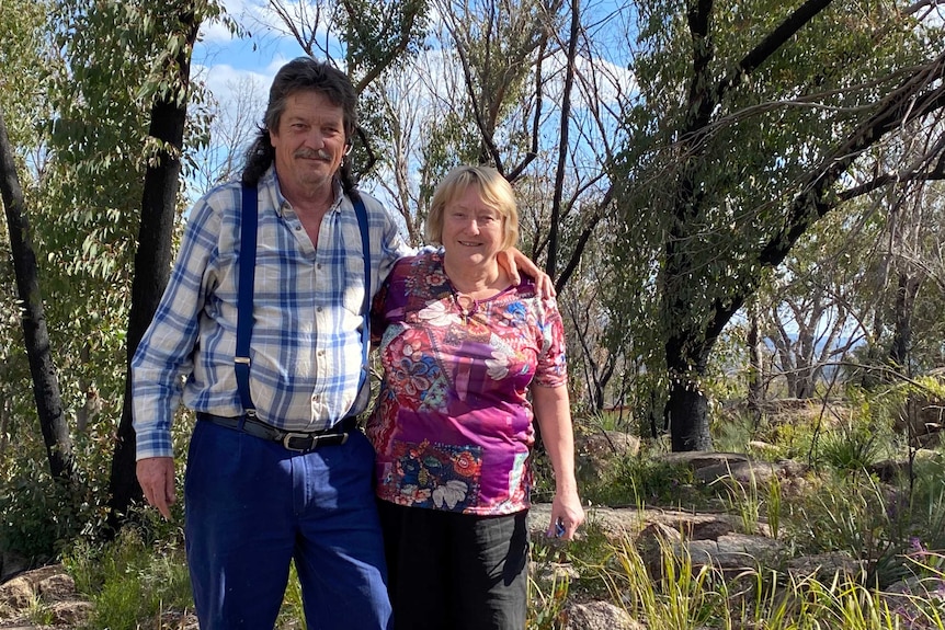 A man and a woman stand in front of a bush garden