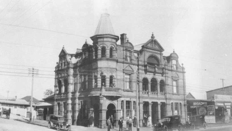 A black and white photo of a hotel. There are old-fashioned buggy cars in the foreground.