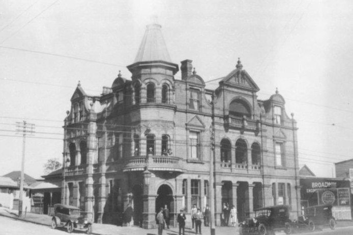 A black and white photo of a hotel. There are old-fashioned buggy cars in the foreground.