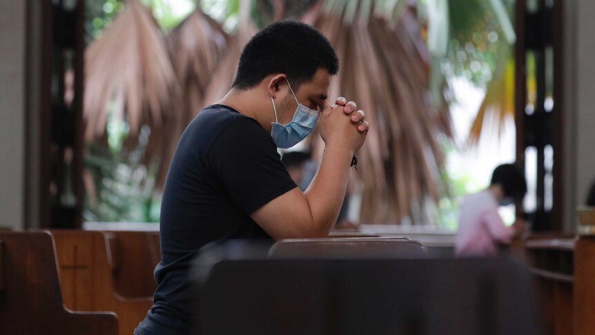 A man wearing a face mask prays in a church with only a few other devotees.