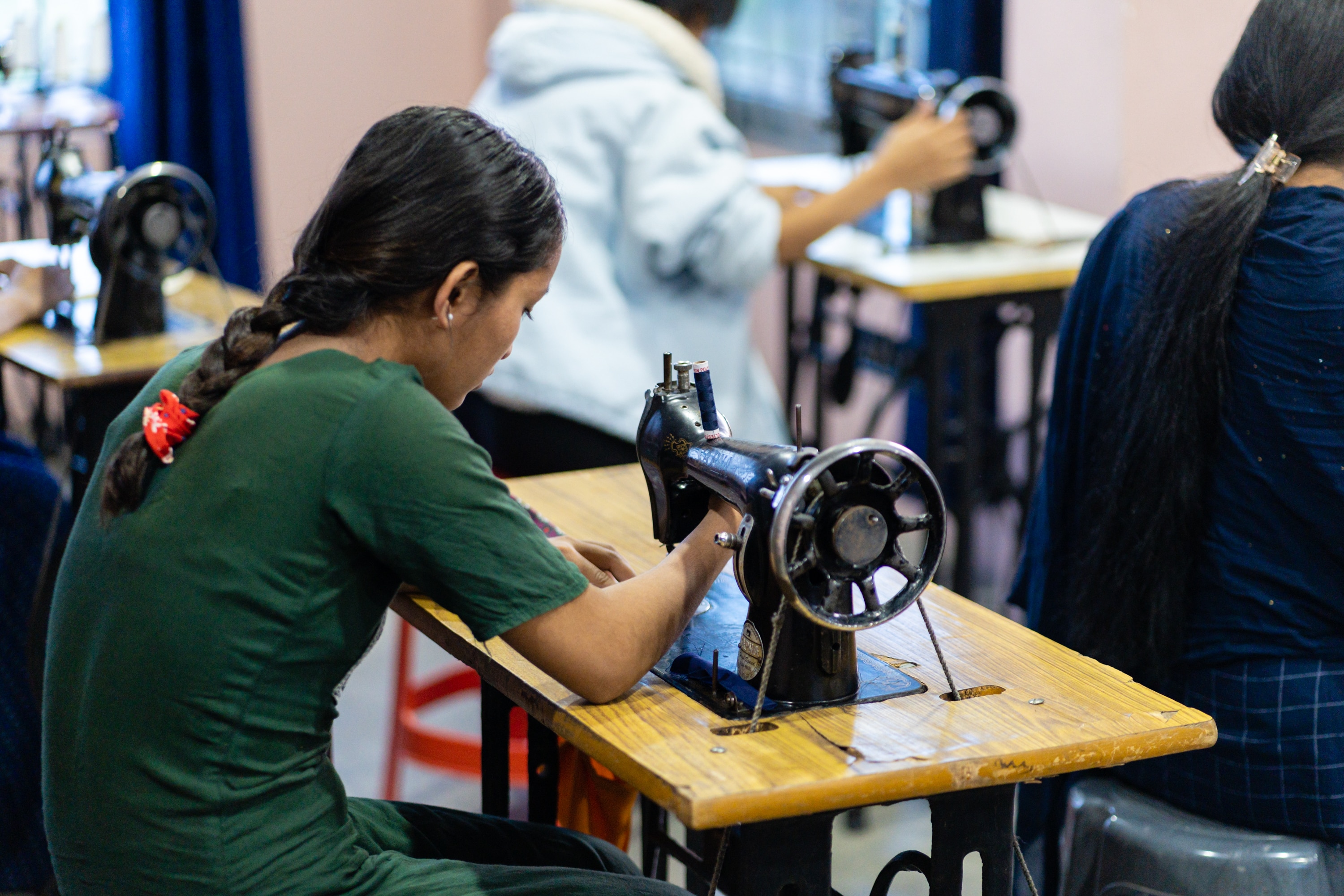 Menina nepalesa usando uma máquina de costura em uma sala com outras pessoas fazendo o mesmo. 