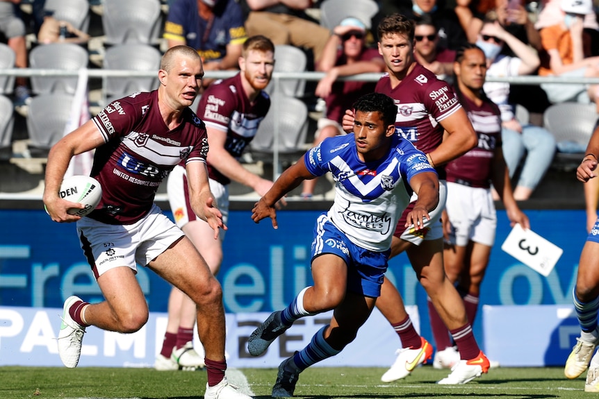 A man in a maroon rugby league jumper runs with football.