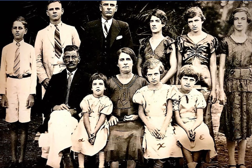 A 1930s sepia family photo of 11 people, including men and women, old and young