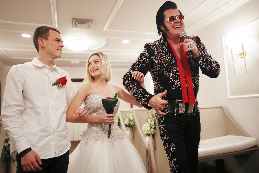 An Elvis impersonator speaking into a microphone stands next to a man and a woman getting married