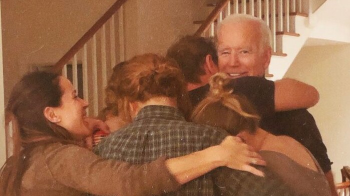 Joe Biden looks at the camera and smiles as his family embraces him in a group hug.