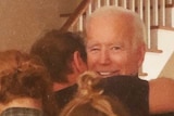 Joe Biden looks at the camera and smiles as his family embraces him in a group hug.