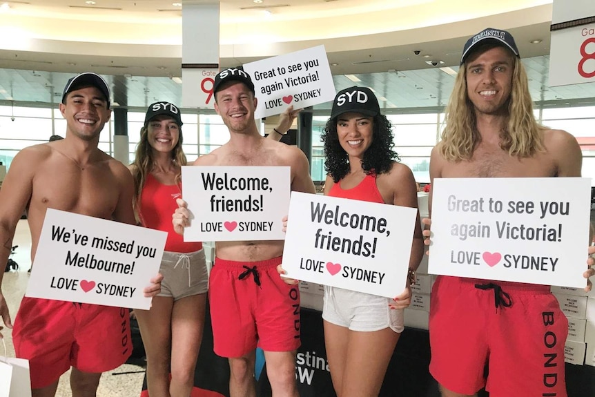 Five life guards stand at the airport with welcome signs
