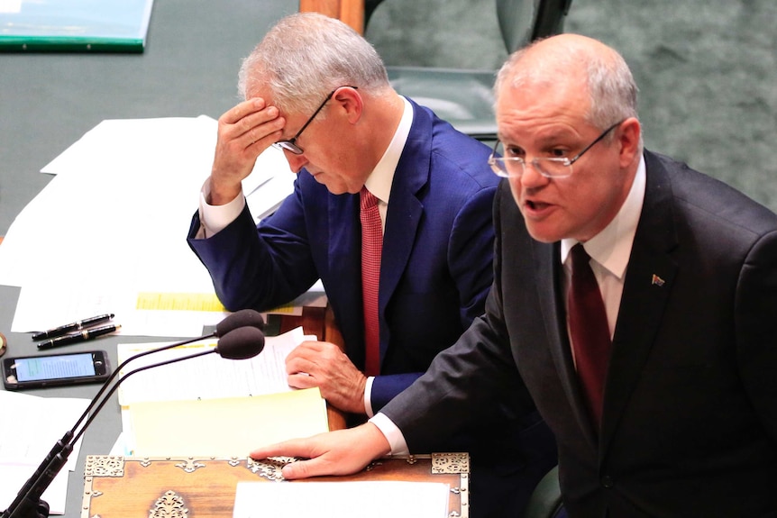 PM Malcolm Turnbull holds his forehead reading, as Treasurer Scott Morrison addresses Parliament.