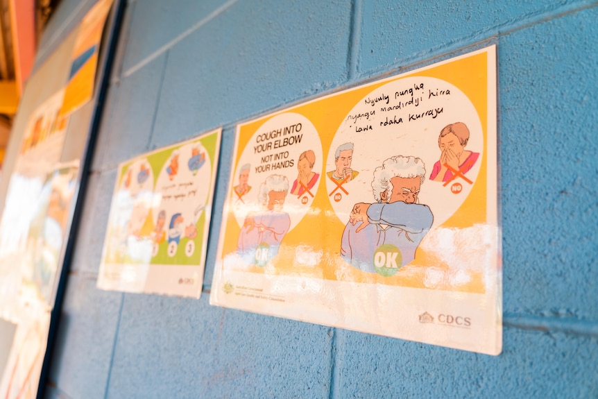 A public health sign demonstrating how to cough safely is seen on a wall.