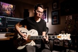 A man with glasses play the guitar in a recording studio