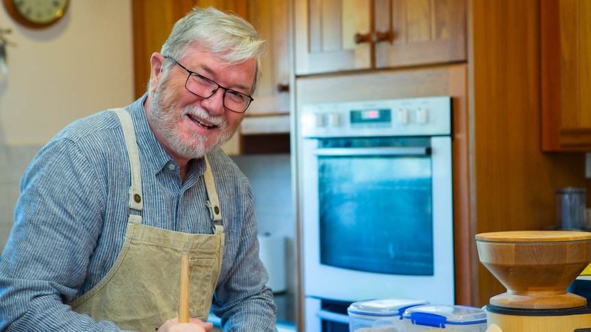 A man smiling in the kitchen as he mixes with a wooden spoon