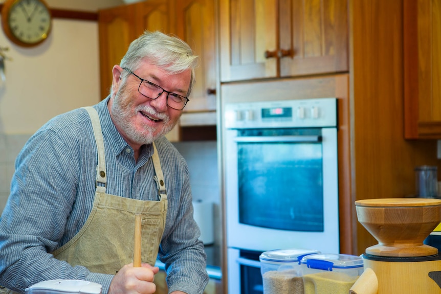A man smiling in the kitchen as he mixes with a wooden spoon