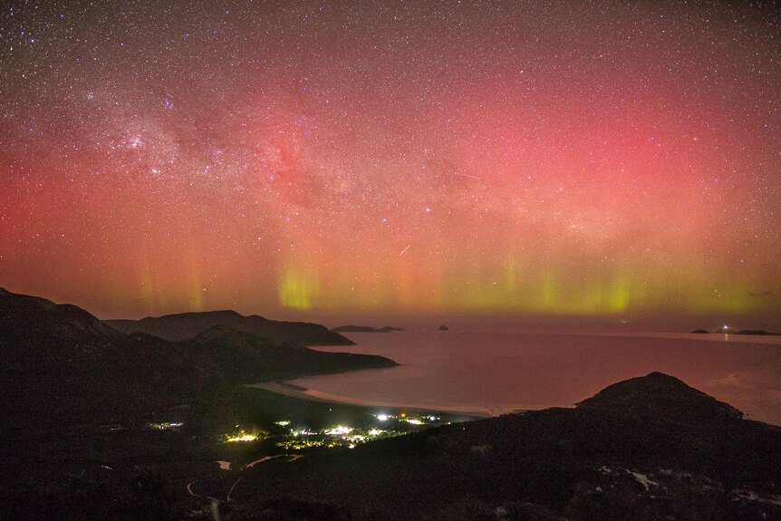 Red and green lights in the starry night sky at a beach in Wilson's Prom with a town nestled between the mountains