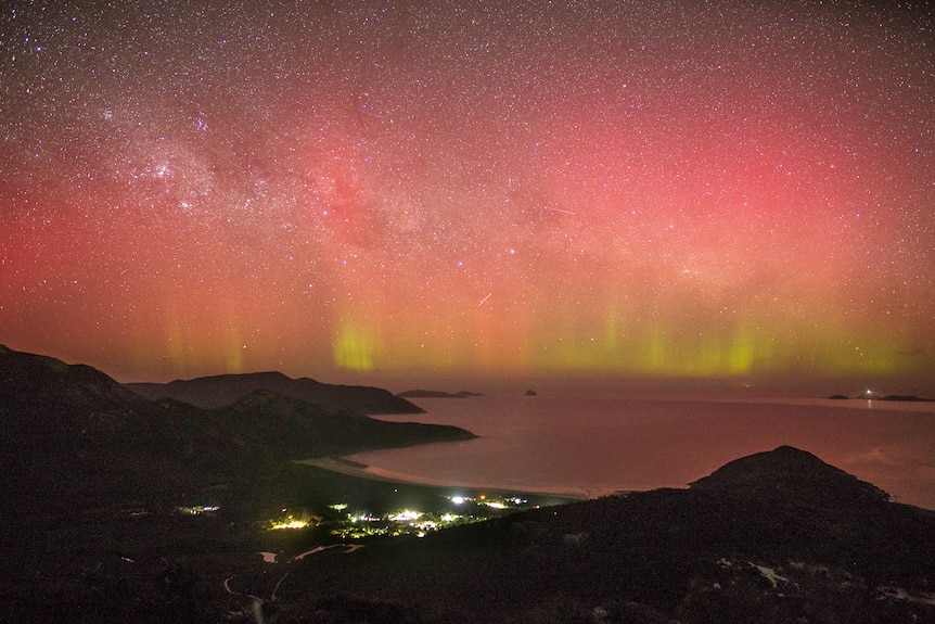 Red and green lights in the starry night sky at a beach in Wilson's Prom with a town nestled between the mountains