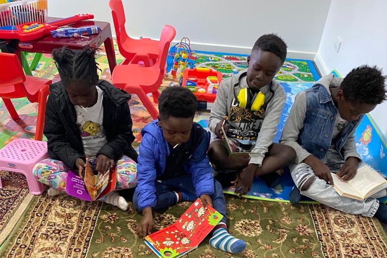 Four of the Turgem children sit together with books on a carpet surrounded by colourful plastic chairs.