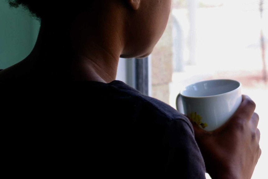 A photo in profile from behind of a woman looking out a window.