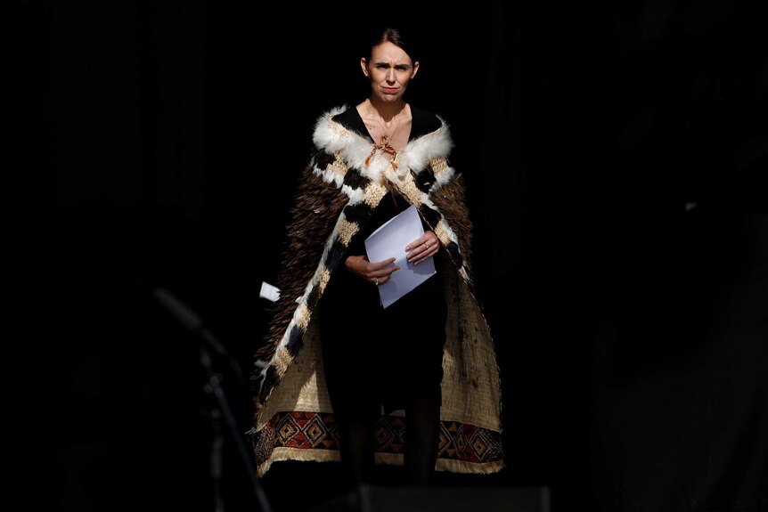 Jacinda Ardern stands on stage holding speech notes dressed in traditional garb