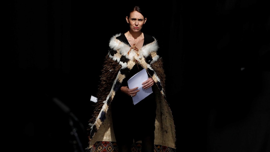 Jacinda Ardern stands on stage holding speech notes dressed in traditional garb