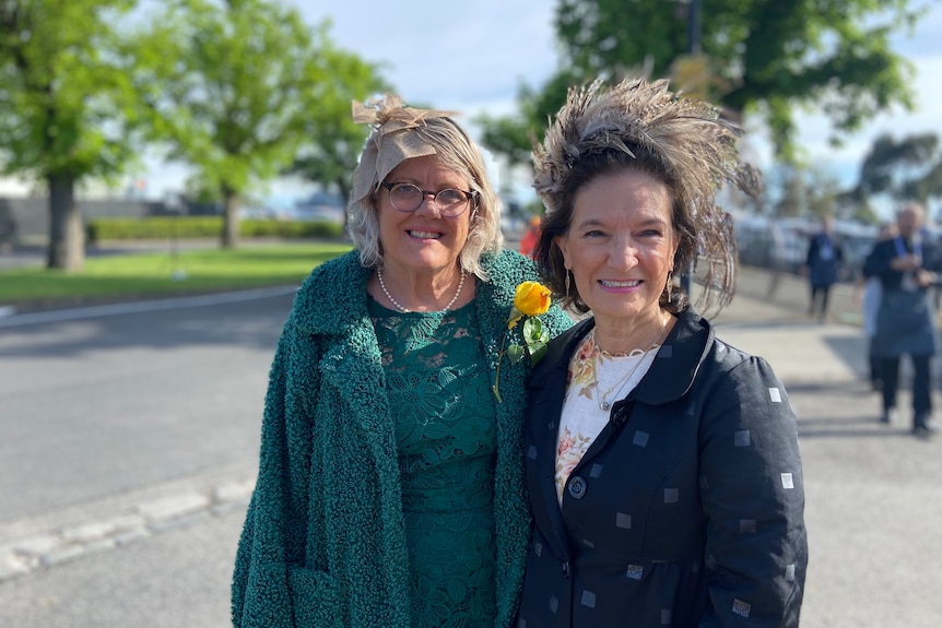 Two women smile, wearing fascinators.