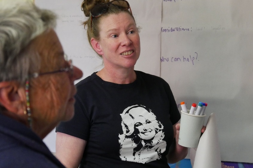 a woman stands wearing a Dolly Parton t-shirt, with sunnies on her head, holding a jar of pens