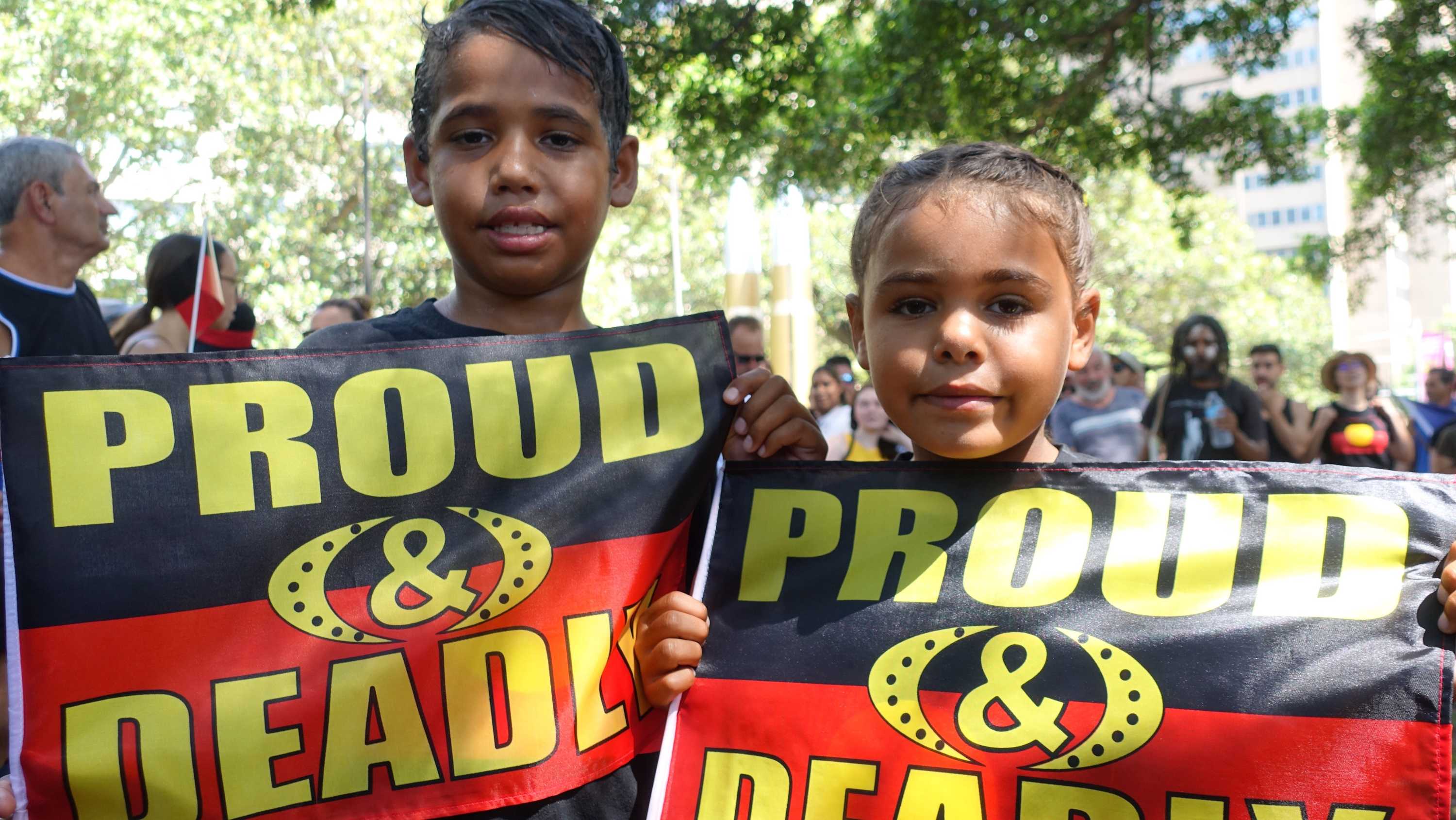 Dos niños sostienen banderas aborígenes con las palabras 