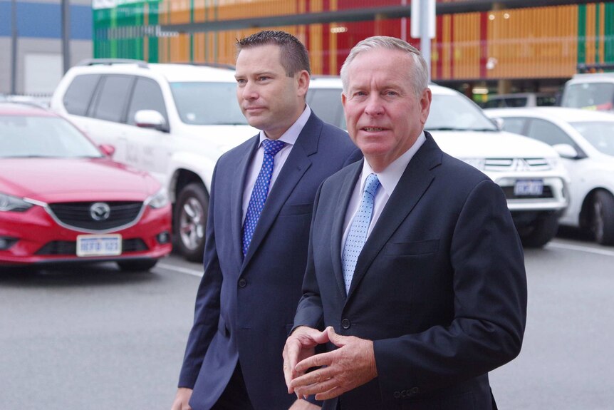 Colin Barnett walks through a car park in a suit with another man behind him.
