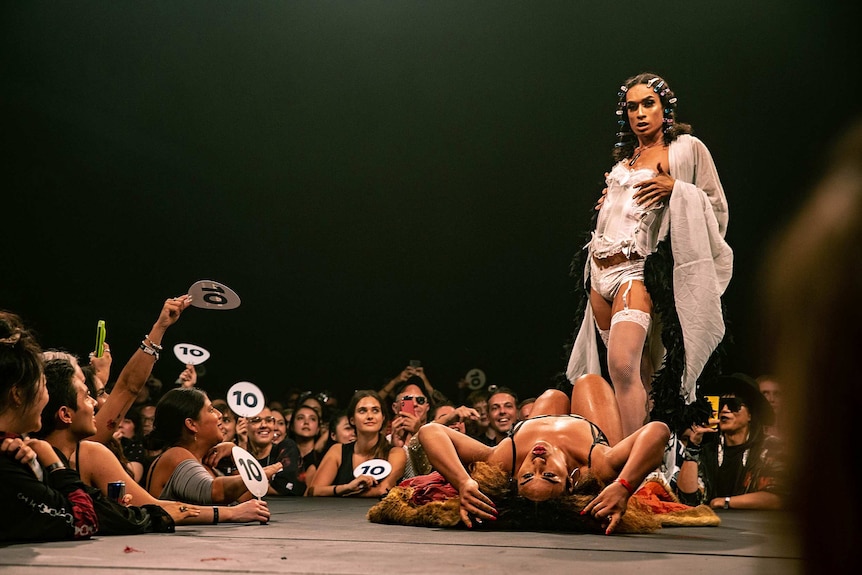 Colour photo of Kilia Tipa lying on back next to a standing dancer on stage at Sissy Ball 2019.