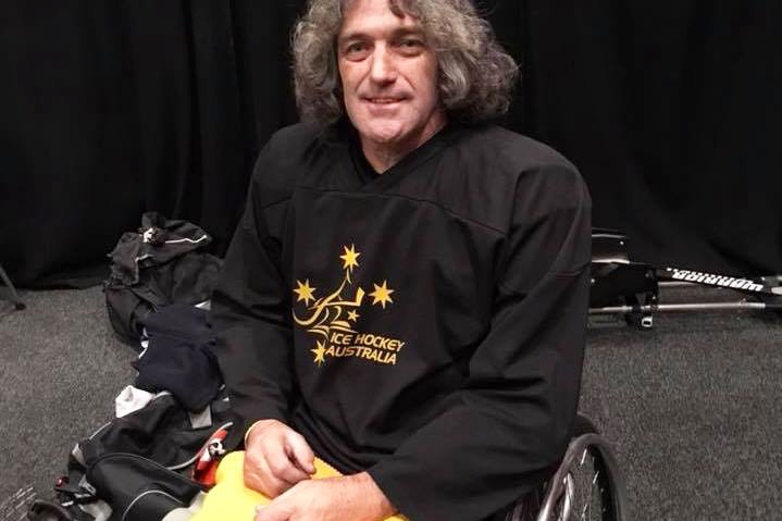 Australian Para-ice hockey athlete Darren Belling smiles in his wheelchair, dressed in his Ice Hockey Australia uniform.