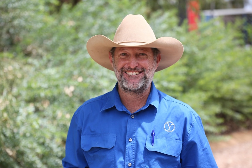 A man wearing a broad-brimmed hat and a blue shirt smiles. 