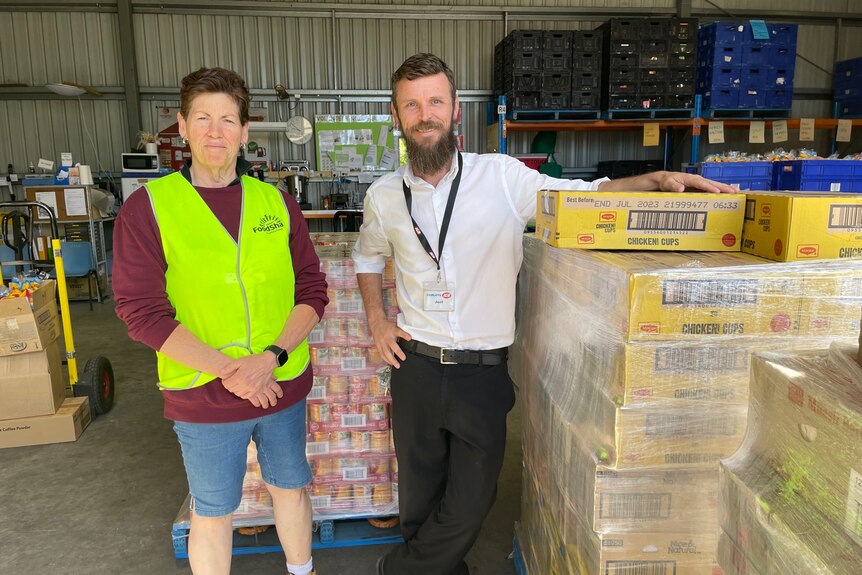 Two people standing near pallets of packaged food, ready to be distributed.