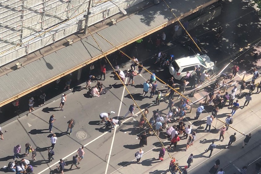 People gathering around a car crash on Flinders Street are seen from above.
