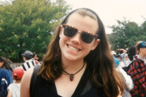 A teenage girl wearing sunglasses smiles for a photo.