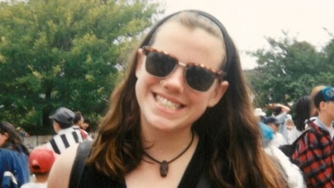 A teenage girl wearing sunglasses smiles for a photo.