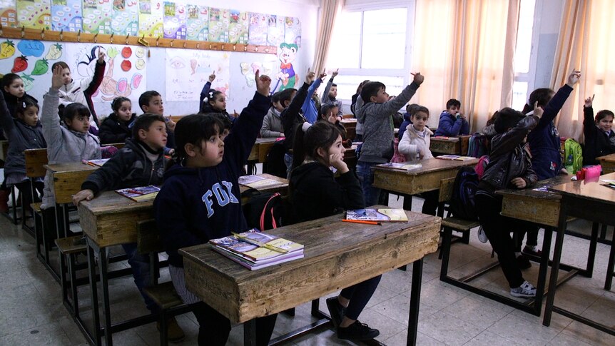 Primary school aged children raise their hands in class