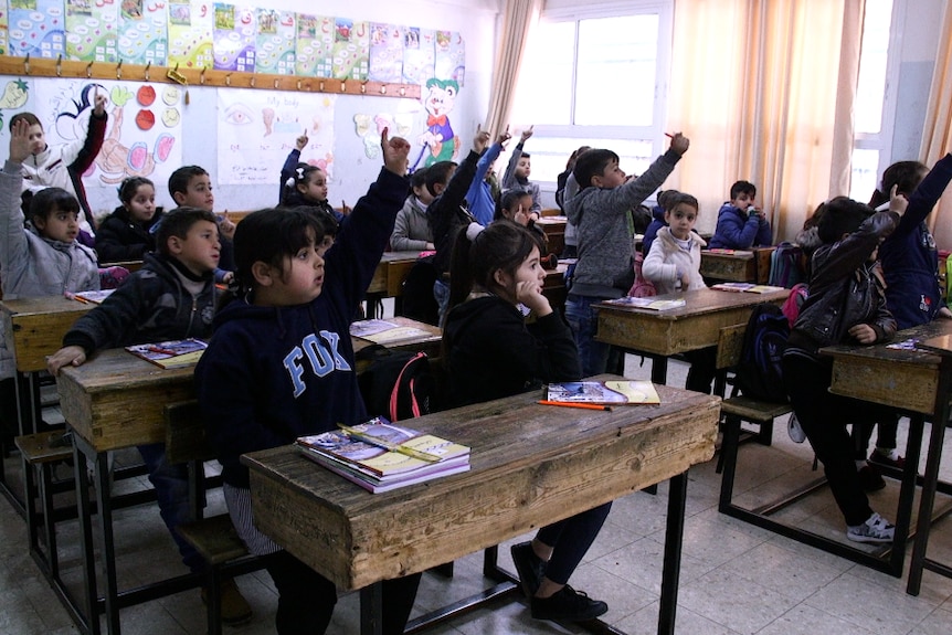 Primary school aged children raise their hands in class