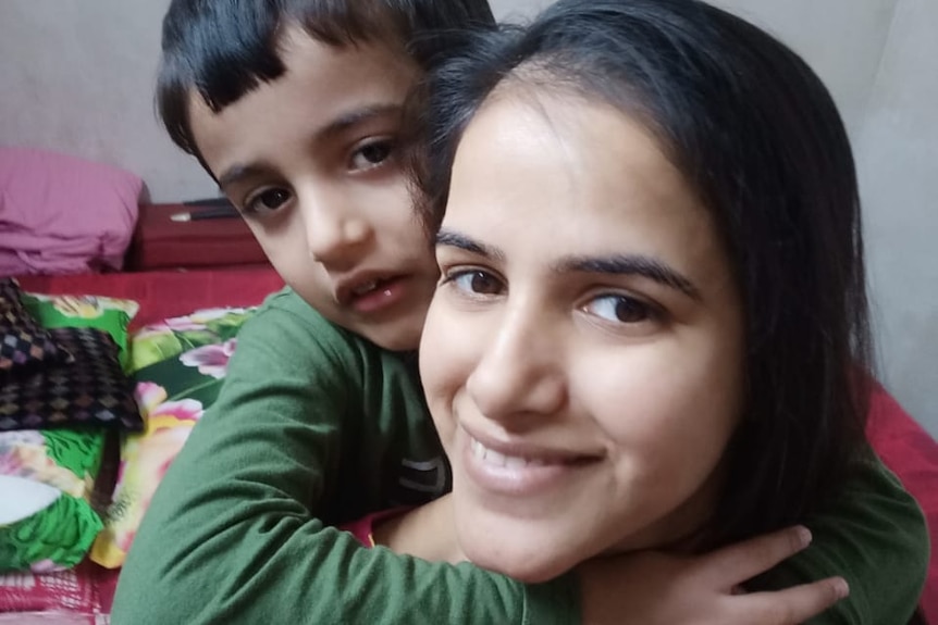 Woman smiling at camera while a little boy hugs her from behind.