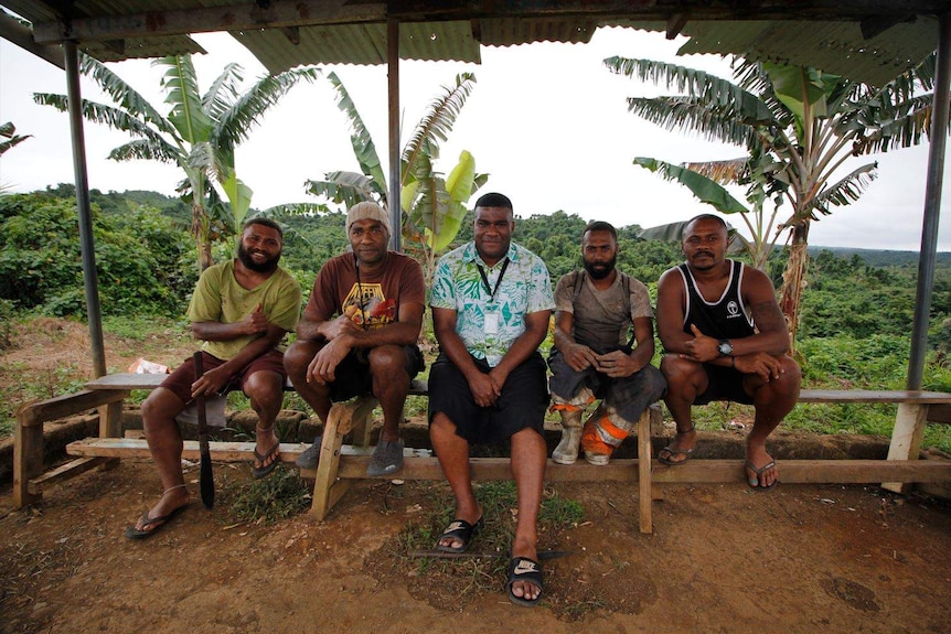 Fijian Broadcasting Corporation reporter Josaia Nanuqa happily sitting outside with four community members