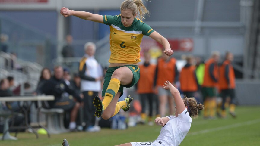 A Matildas player leaps high to avoid having her legs taken out by a tackle.