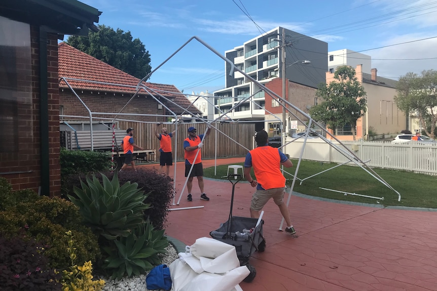 Four men in orange hi-vis vests set up structure of a marquee tent