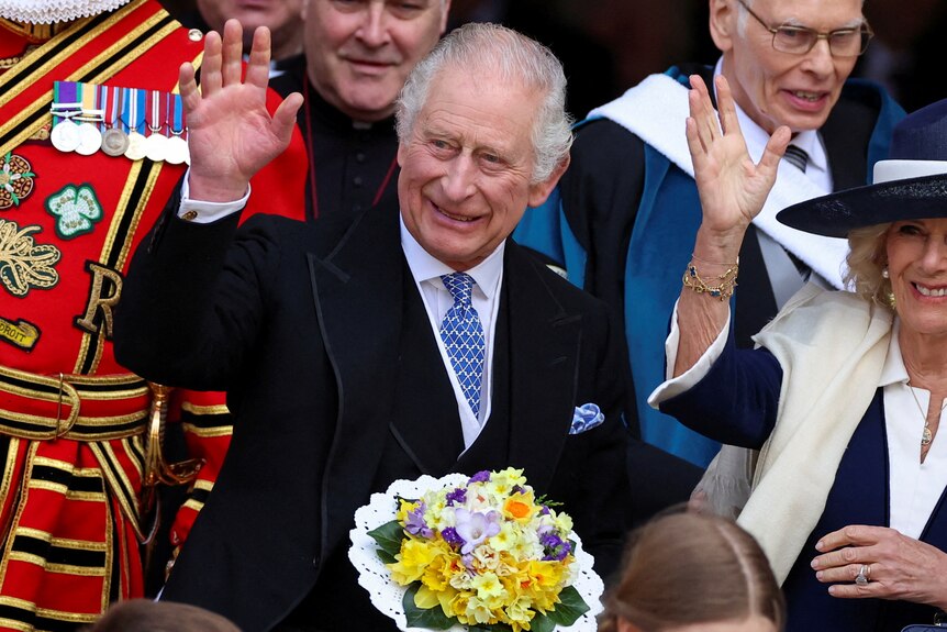 Charles stands on steps next to camilla holding a bouquet of flowers. 