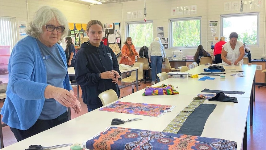 A woman points to fabric with an Aboriginal design next to a student looking curiously. 