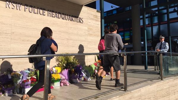 NSW police employees walk past floral tributes at Parramatta Police HQ