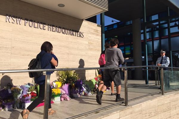 NSW police employees walk past floral tributes at Parramatta Police HQ